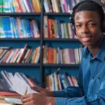 Male Teenage Student Working At Computer Wearing Headphones