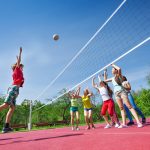 Teenagers play volleyball game on playing ground