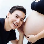 Expectant husband listening to pregnant woman wife over isolated white background